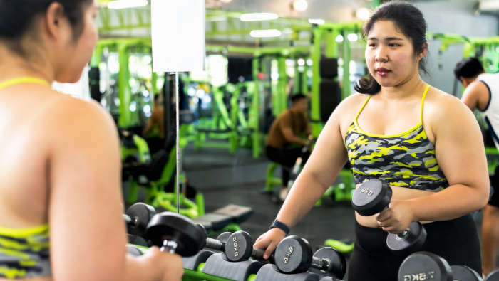 Abnehmen mit Krafttraining: Eine Frau mit Kurzhanteln vor einem Spiegel