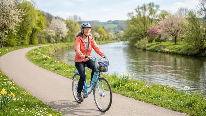 Eine Frau fährt in einer Frühlingslandschaft gemütlich Rad entlang eines Flusses